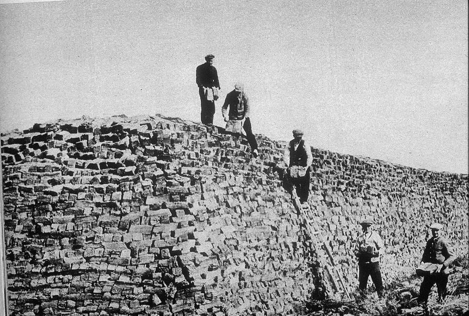 Oude zwartwitfoto van turfstekers die op en naast grote stapel turf staan