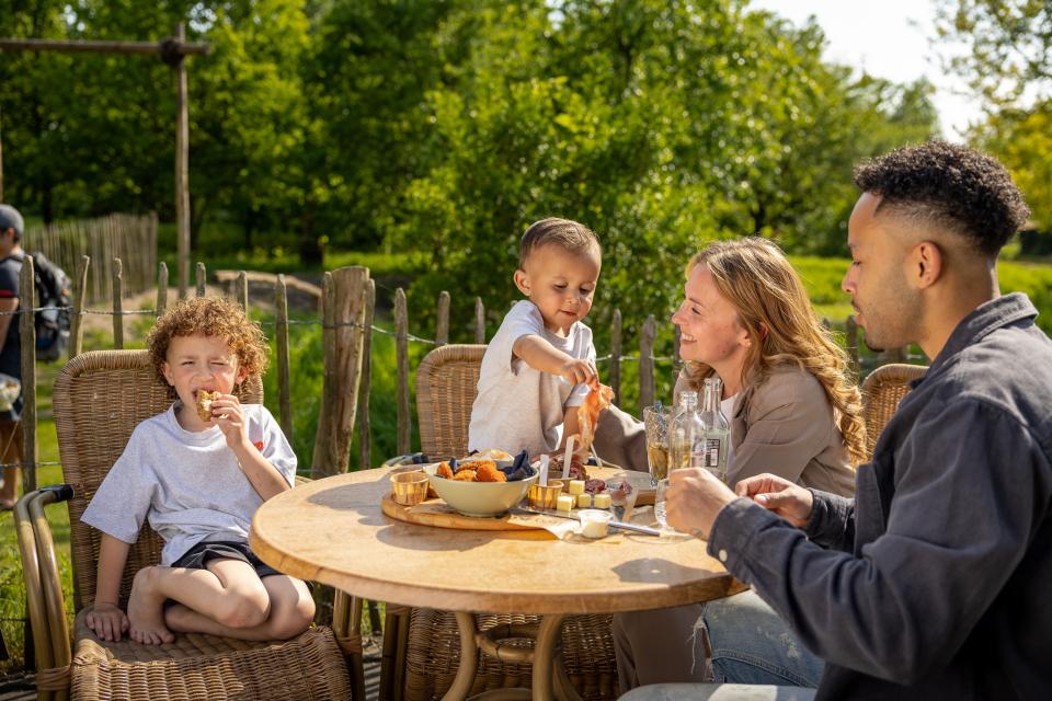 Twee kinderen en volwassenen met borrelplank aan tafel op terras in natuurlijke omgeving
